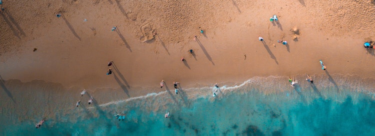 Aerial drone shot of people on beach. Summer concept, bright blue water, sand.