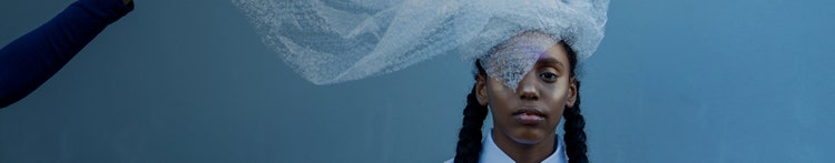 Moody portrait of young black girl in braids with bubble wrap as a veil on top of her head.