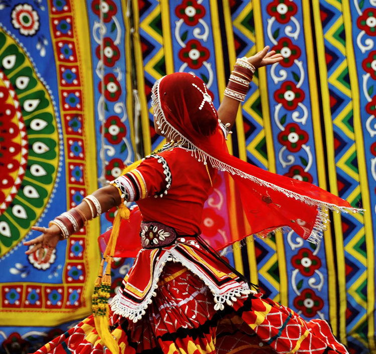 Female dancer in traditional Southeast Asian attire performs on stage decorated in traditional patterns.